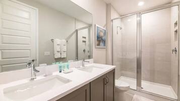 A bathroom with a double sink vanity, a toilet, and a glass-enclosed shower.