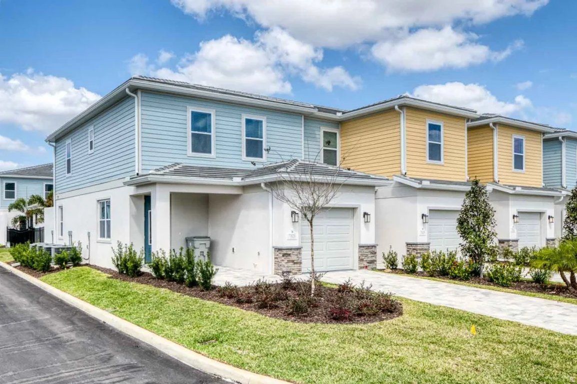 A row of townhouses with a front yard, a driveway, and a clear sky.
