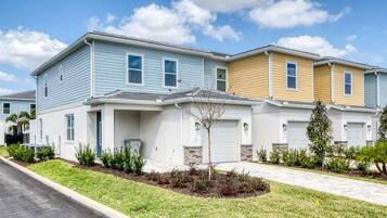 A row of townhouses with a front yard, a driveway, and a clear sky.