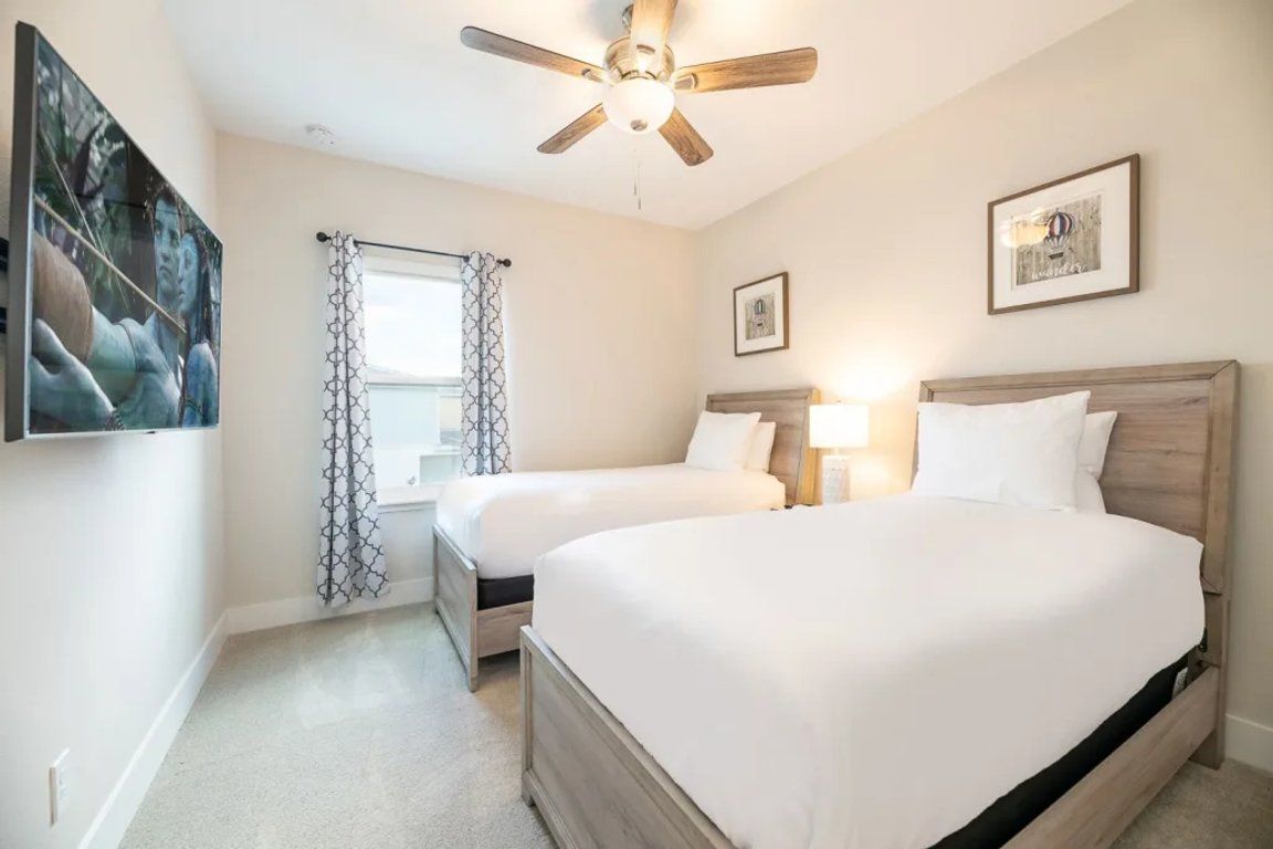 A bedroom with two beds, a ceiling fan, and a window with patterned curtains.