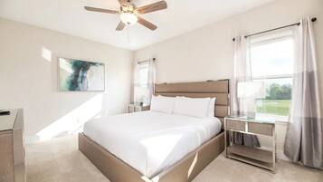 Une chambre d’hôtel moderne avec un grand lit, un ventilateur de plafond, une table de chevet et une fenêtre avec des rideaux.