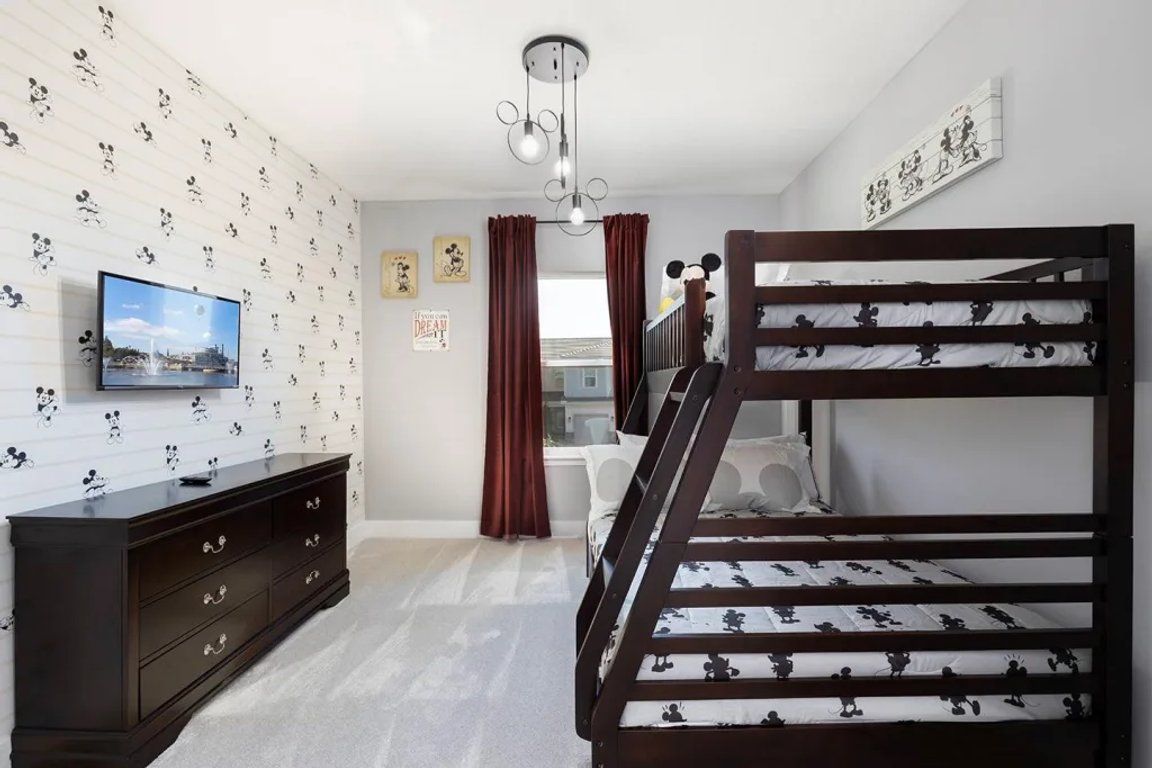 Une chambre avec un lit superposé, une télévision, une commode et un papier peint à motifs de Mickey Mouse.