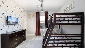 Une chambre avec un lit superposé, une télévision, une commode et un papier peint à motifs de Mickey Mouse.