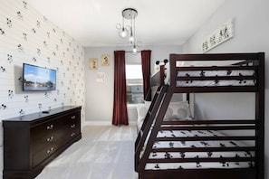 Una camera con un letto a castello, una televisione, un comò e carta da parati a tema Topolino.