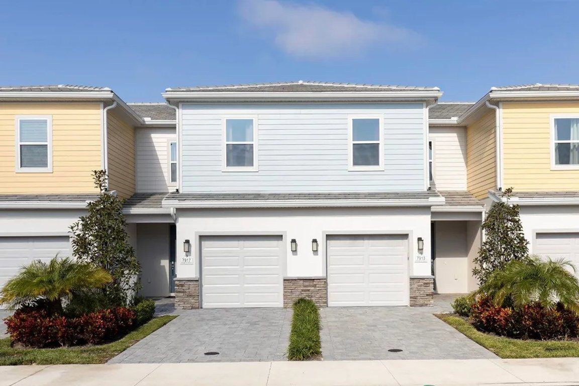 Une rangée de maisons de ville, chacune avec deux garages, une pelouse devant et un ciel dégagé.