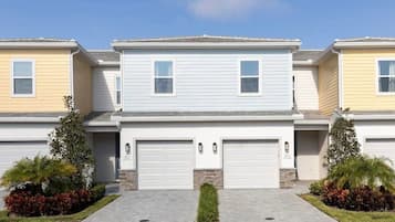 Une rangée de maisons de ville, chacune avec deux garages, une pelouse devant et un ciel dégagé.