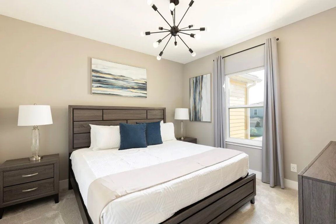 A bedroom with a large bed, two bedside tables with lamps, a modern ceiling light, and a window with curtains.