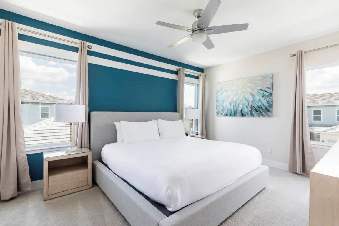 A hotel room with a bed, a nightstand, a ceiling fan, and a window with curtains.