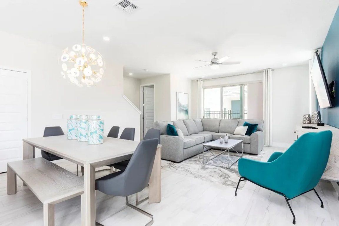 Un salon moderne comprenant un coin repas, un canapé gris, un fauteuil turquoise et un lustre.