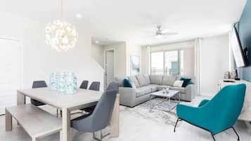Un salon moderne comprenant un coin repas, un canapé gris, un fauteuil turquoise et un lustre.
