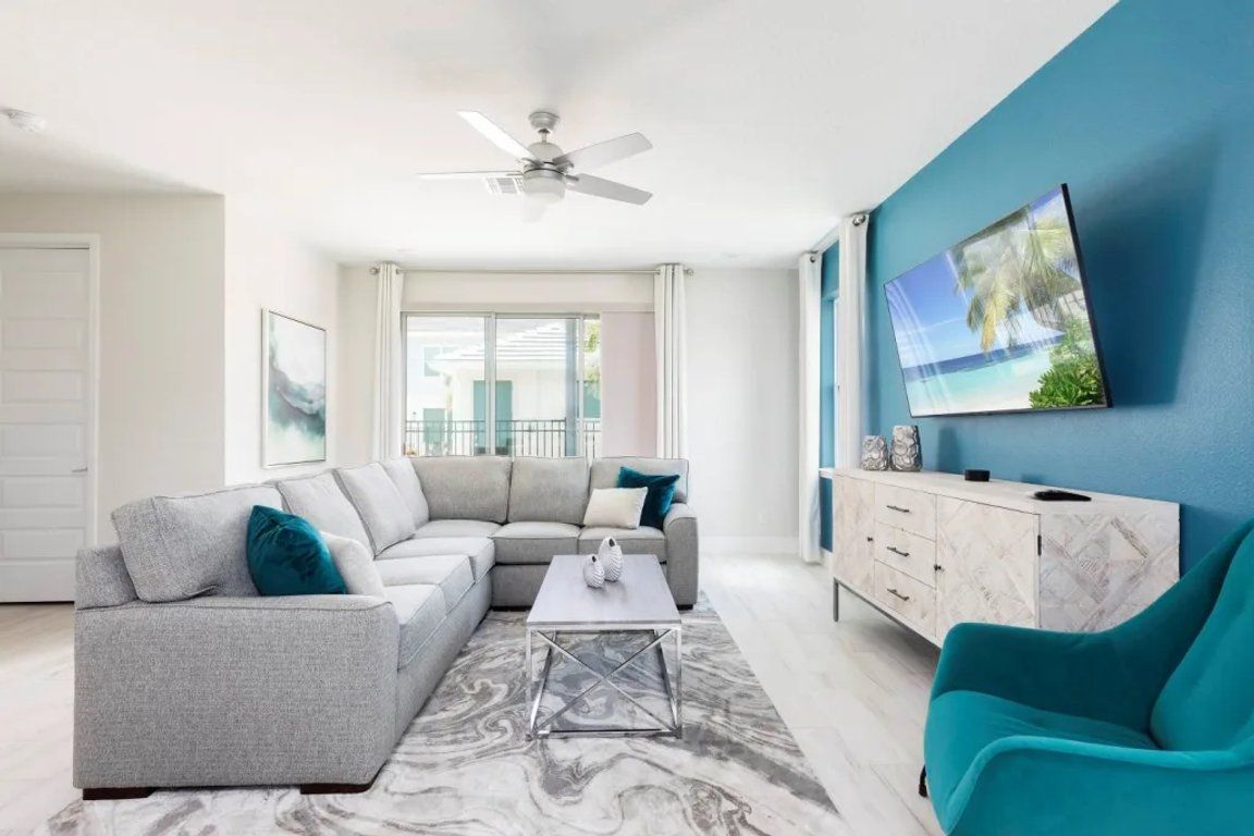 A modern living room with a grey sectional sofa, a teal armchair, a marble coffee table, and a white cabinet.
