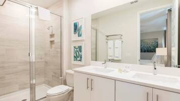 A modern bathroom with a glass shower enclosure, a white toilet, and a large mirror above a double sink vanity.