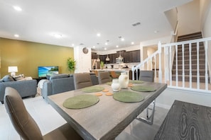 A modern living room with a dining area, a kitchen in the background, and a staircase. - Windsor Island - 7711 (Davenport)