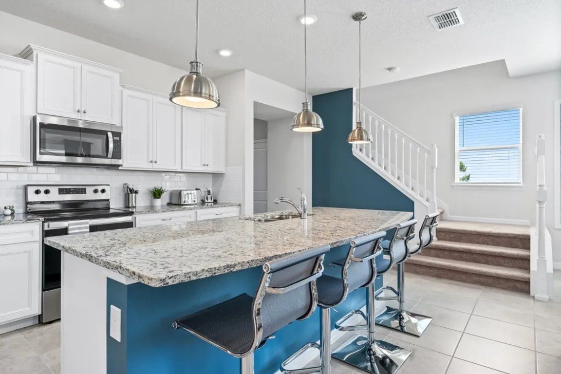 A modern kitchen with white cabinets, stainless steel appliances, a blue accent wall, and bar stools.