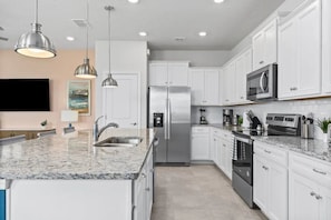 A modern kitchen with white cabinetry, stainless steel appliances, granite countertops, pendant lighting, and a flat-screen TV mounted on the wall. - Windsor Island - 7897 (Davenport)