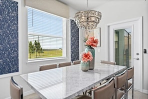 A dining area with a marble table, chairs, a chandelier, and a window with blinds. - Windsor Island - 7897 (Davenport)