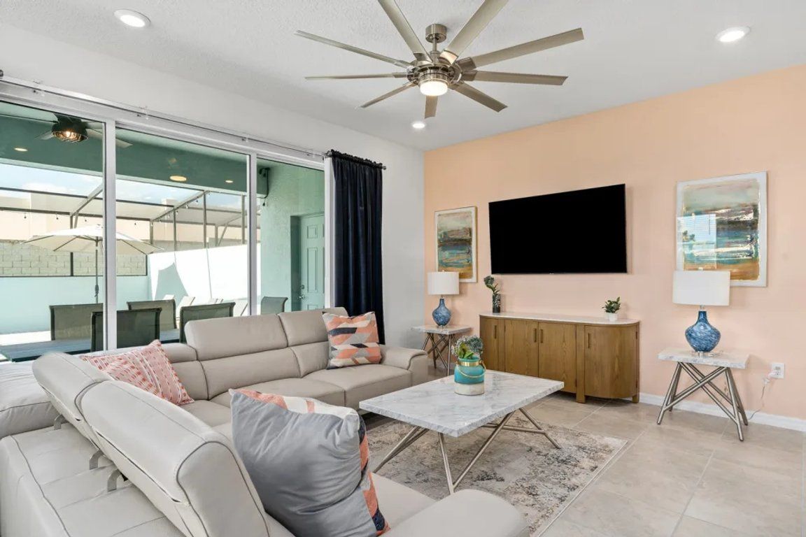 A modern living room with a ceiling fan, a flat-screen TV, a sofa set, a coffee table, and a view through a glass door.