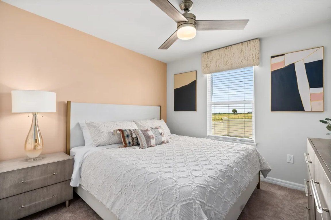 A bedroom with a bed, a nightstand, a ceiling fan, and artwork on the walls.