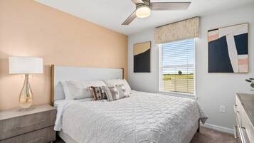 A bedroom with a bed, a nightstand, a ceiling fan, and artwork on the walls.