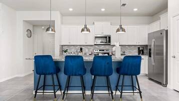Una cocina moderna con armarios blancos, un refrigerador de acero inoxidable, un microondas y cuatro taburetes azules.