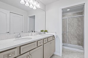 A bathroom with a double sink vanity, a large mirror, and a shower area. - Windsor at Westside - 7899 (Kissimmee)