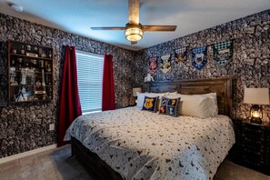 A bedroom with a stone wall, a wooden headboard, a ceiling fan, a bedside table with a lamp, and a window with red curtains. - Windsor Island - 8077 (Davenport)