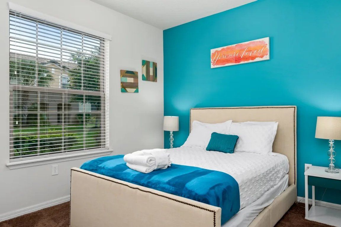 A bedroom with a bed, a window with blinds, a teal accent wall, and a sign with the word 'Inspired'.