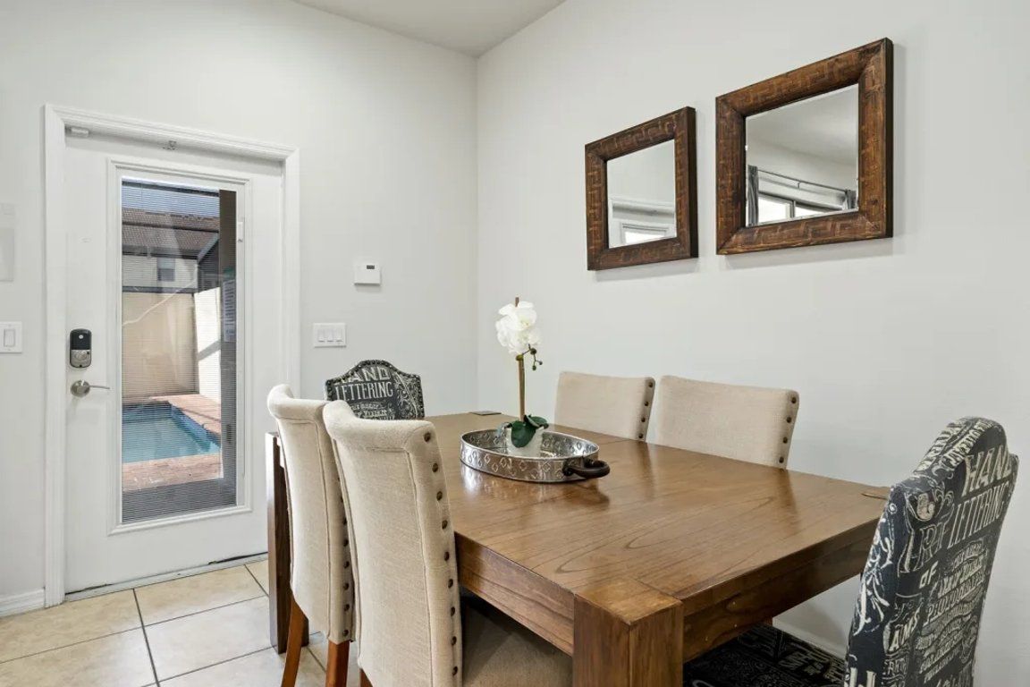 A dining area with a wooden table, four chairs, two wall-mounted mirrors, and a decorative tray with a white flower.