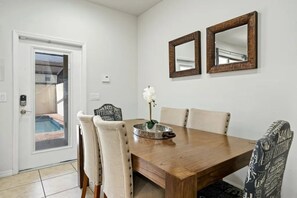 A dining area with a wooden table, four chairs, two wall-mounted mirrors, and a decorative tray with a white flower. - Windsor at Westside - 8106 (Kissimmee)