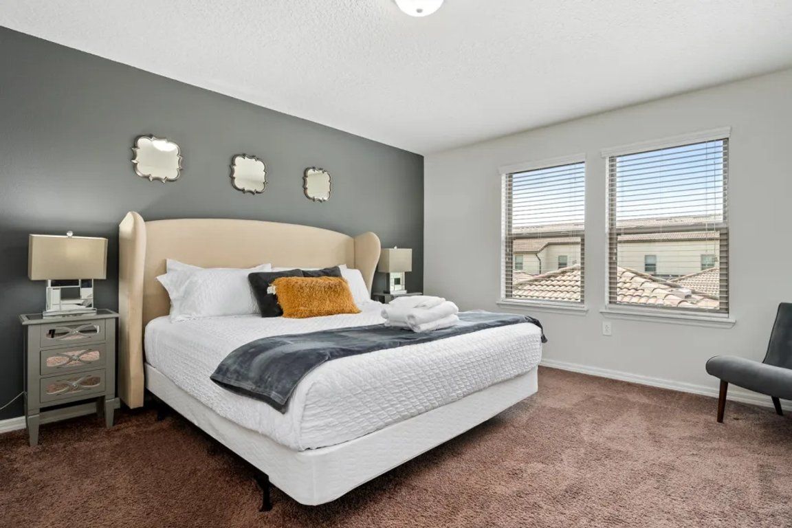 A bedroom with a bed, nightstands, a chair, and a window with blinds.