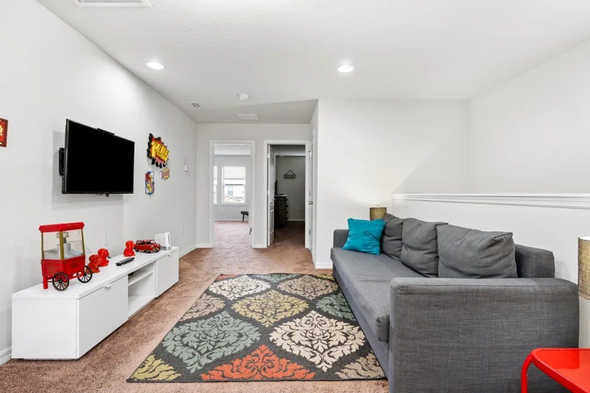 A modern living room with a grey sofa, a flat-screen TV mounted on the wall, and a white entertainment unit with toys.