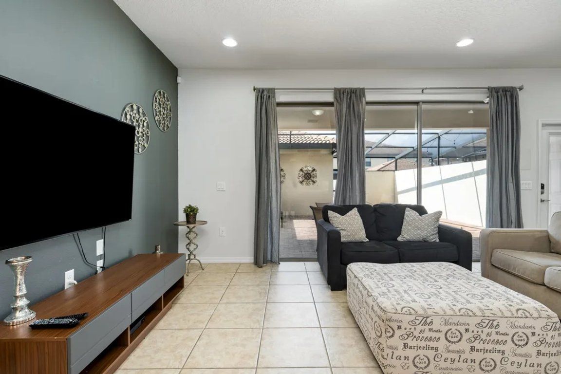 A modern living room with a flat-screen TV, a sofa, a coffee table, and a patterned ottoman.