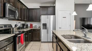 A modern kitchen with stainless steel appliances, dark cabinetry, and a granite countertop.