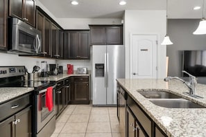 A modern kitchen with stainless steel appliances, dark cabinetry, and a granite countertop. - Windsor at Westside - 8106 (Kissimmee)