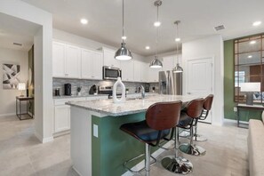 Una cocina moderna con armarios blancos, encimera de granito, electrodomésticos de acero inoxidable e iluminación colgante.
