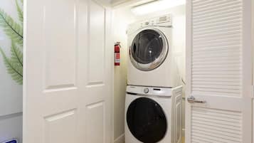 Un lavadero con lavadora y secadora apiladas, un extintor y una puerta con panel de vidrio esmerilado.