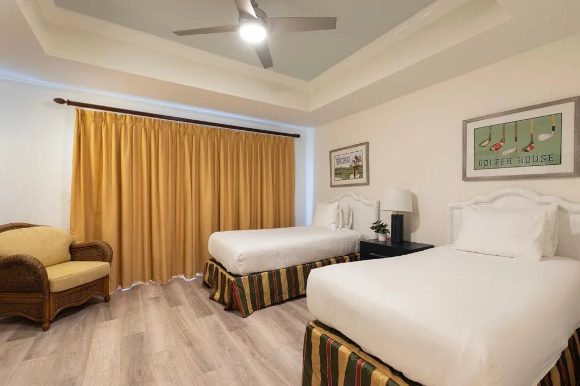 Une chambre d’hôtel avec deux lits simples, un canapé, un ventilateur de plafond et une décoration murale sur le thème du golf.