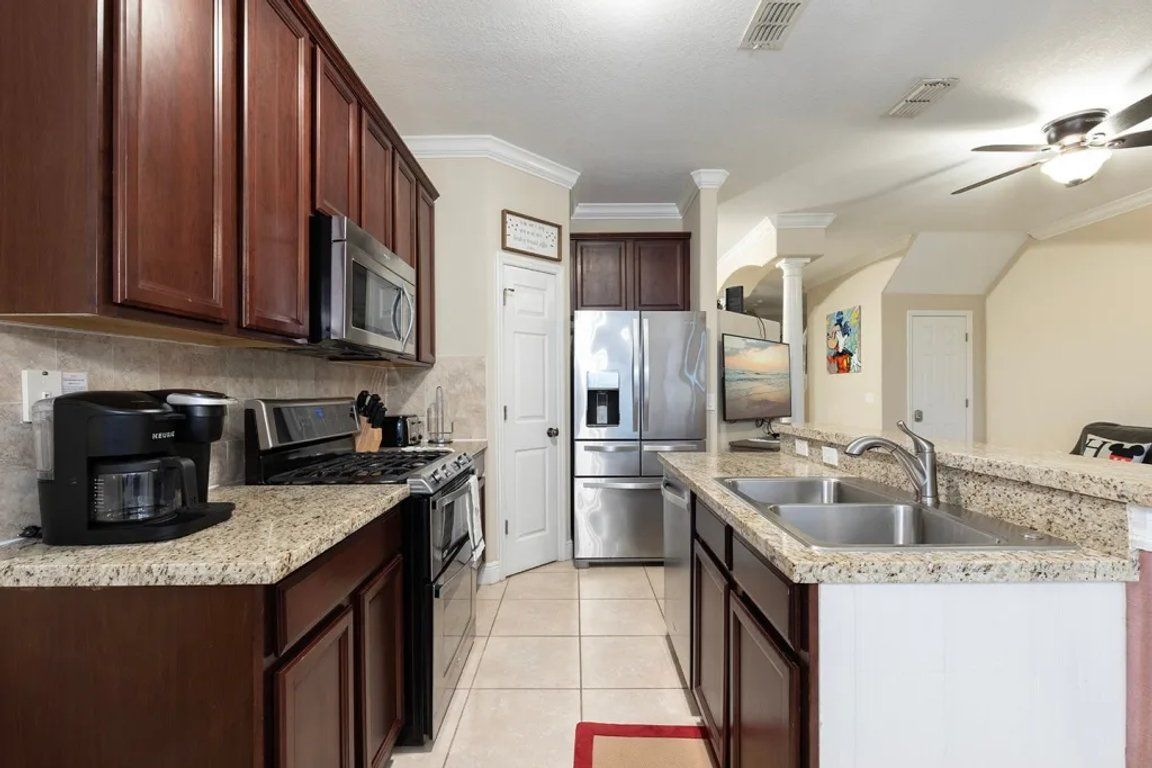 A kitchen with dark wood cabinets, stainless steel appliances, a granite countertop, and a red rug.