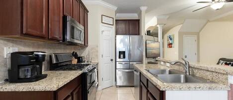 A kitchen with dark wood cabinets, stainless steel appliances, a granite countertop, and a red rug.