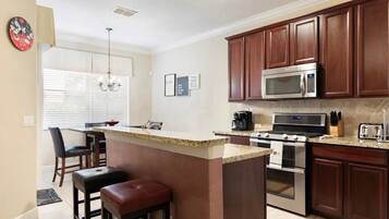 A kitchen with a central island, dark wooden cabinets, stainless steel appliances, and a dining area with a bar stool.