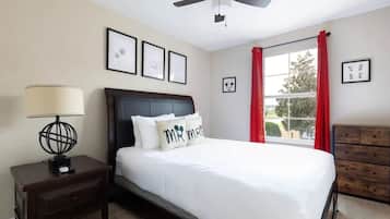 A bedroom with a bed, a nightstand, a dresser, a ceiling fan, and a window with red curtains.
