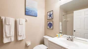 Une salle de bain avec des toilettes, un lavabo et un miroir. Des serviettes sont accrochées au mur et un tableau encadré est placé au-dessus des toilettes.