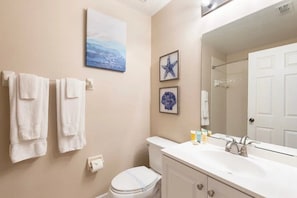Un bagno con il water, un lavandino e uno specchio. Asciugamani appesi al muro e un quadro incorniciato sopra il water.