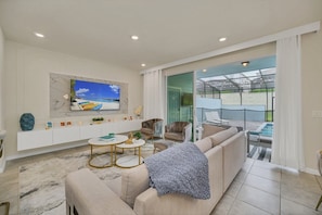 A modern living room with a large TV, comfortable seating, a glass door leading to a balcony with a pool. - Windsor Island - 24627 (Davenport)