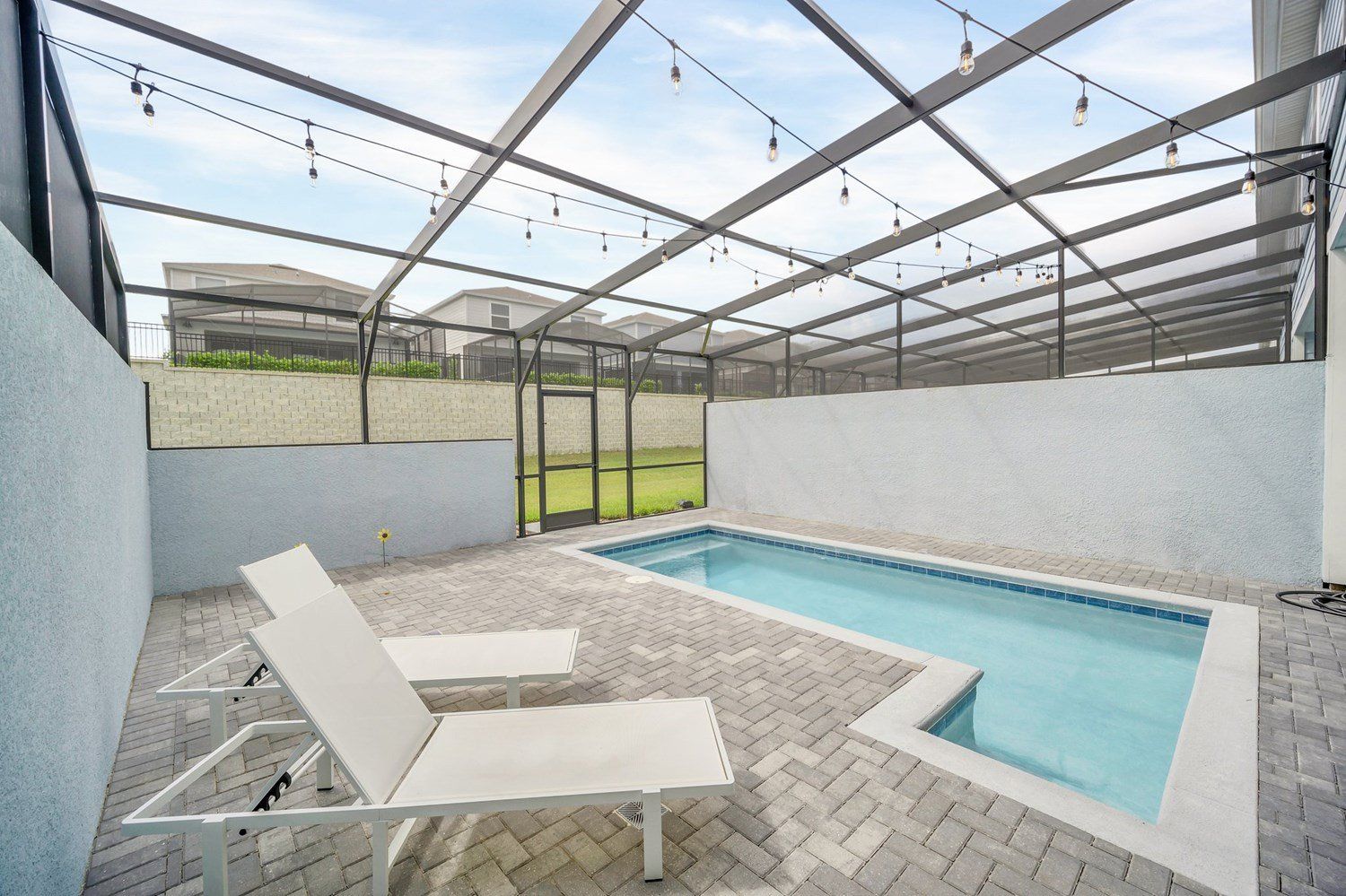 An outdoor swimming pool with a glass ceiling, surrounded by a brick patio and white lounge chairs.