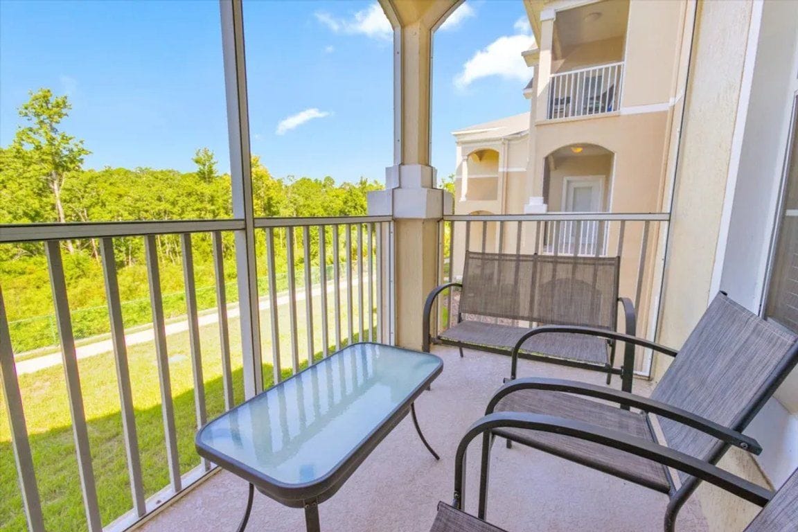 A balcony with a glass table and two chairs, overlooking a green landscape.