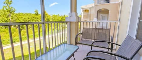 A balcony with a glass table and two chairs, overlooking a green landscape.