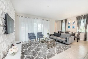 A modern living room with a grey sofa, two patterned armchairs, a coffee table, and a flat-screen TV mounted on a textured wall. - Solara Resort - 25528 (Kissimmee)