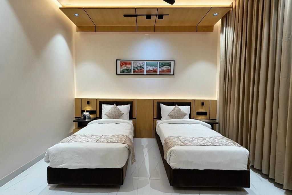 A hotel room with two beds, a ceiling light fixture, a wall-mounted artwork, and a curtain on the window.