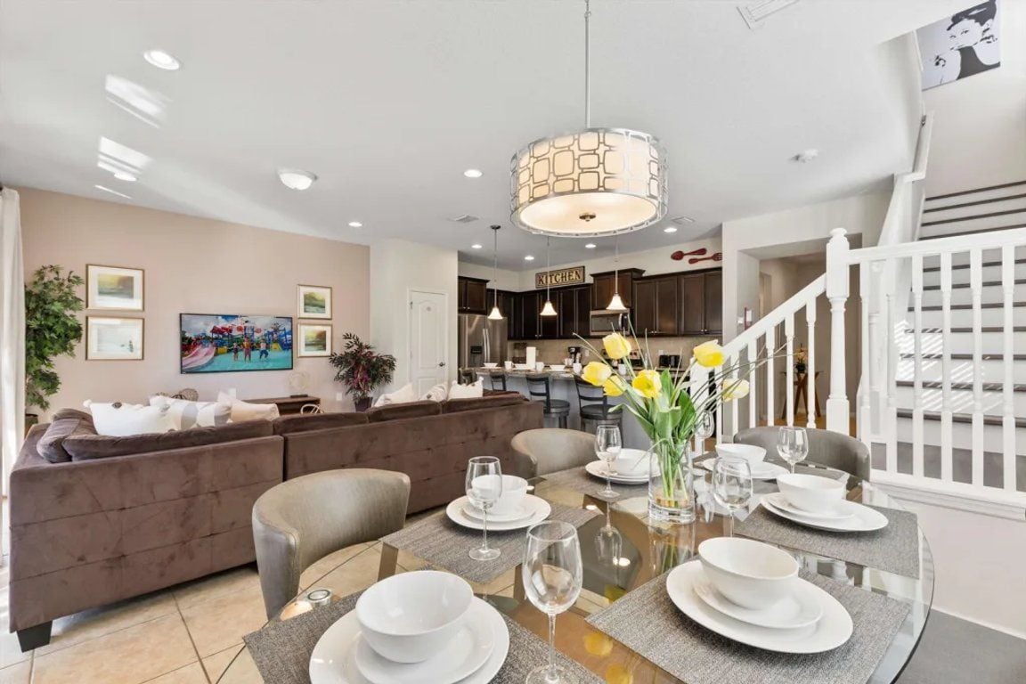 A dining area with a glass table set for six, a modern pendant light, and a kitchen in the background.